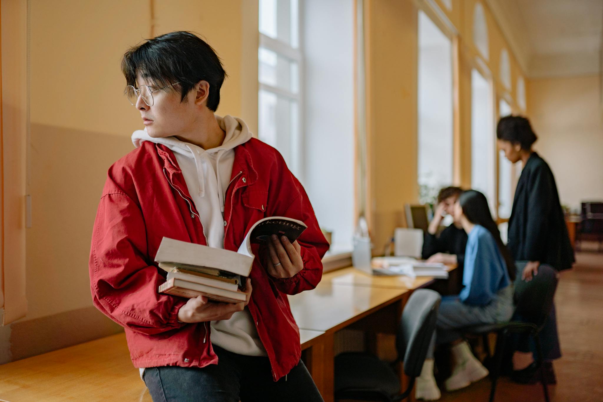 A young adult student holding books in a university library setting.
