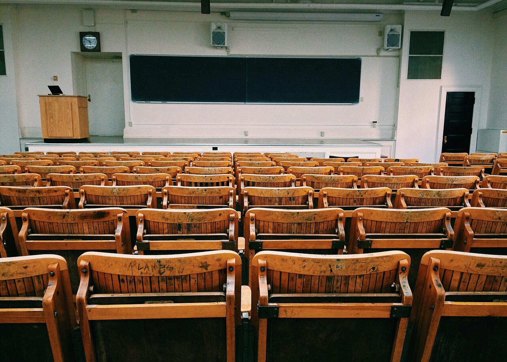 An empty lecture hall featuring wooden chairs and a large blackboard.