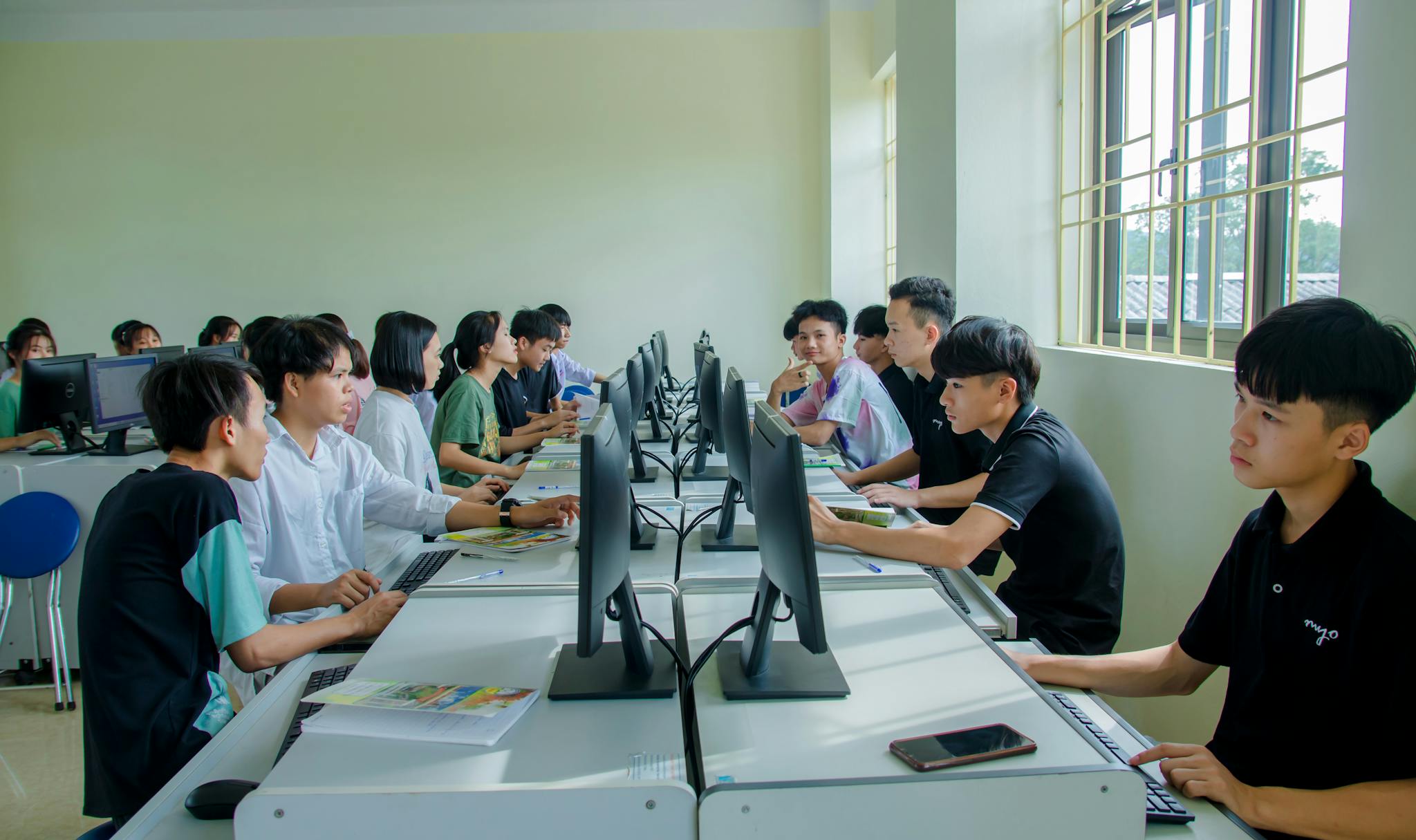 Diverse group of students studying in a computer-equipped classroom setting.